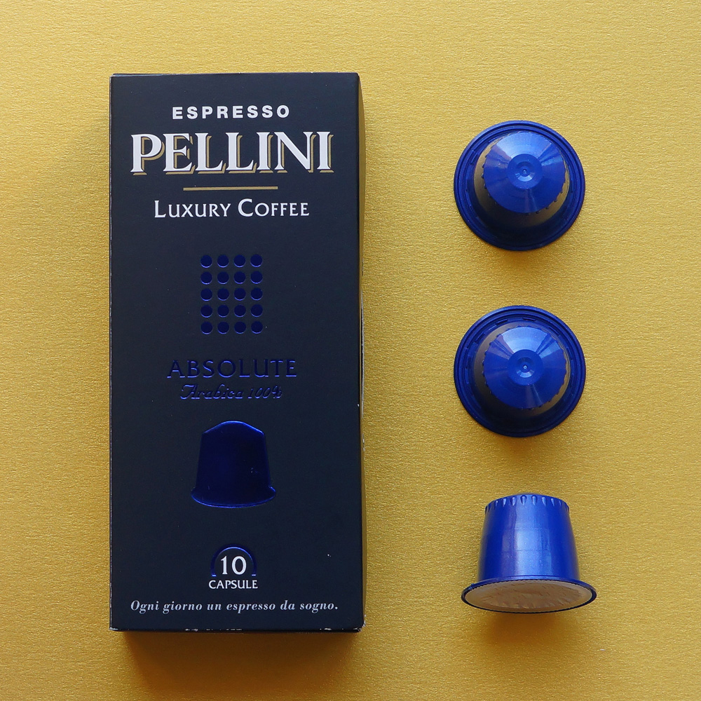 Absolute by Pellini Espresso - three blue coffee capsules with a dark box on golden background