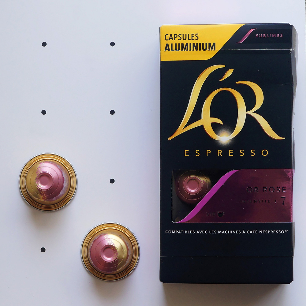 Or Rose L'Or Espresso - two golden pink coffee capsules with a box on a white background